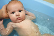 cute little baby swimming in blue bath on father's hands