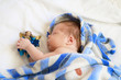 Cute newborn baby sleeping in blue blanket with figure of angel in hands on white background.