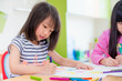 © weedezign - Preschool girl kid drawing with color pencil on white paper on table in classroom with friends and teacher,Kindergarten education concept.