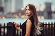 Gorgeous young model woman with perfect blonde hair looking at camera posing in the city wearing black evening dress.