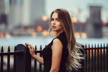 gorgeous young model woman with perfect blonde hair looking at camera posing in the city wearing bla