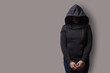 front view of a girl in a black hood with handcuffed hands isolated on a gray