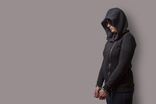 Side View Of A Girl In A Black Hood With Handcuffed Hands Isolated On A Gray