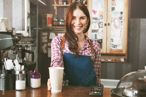 Fotografie, Obraz Young female barista smiling, while serving a coffee at the counter