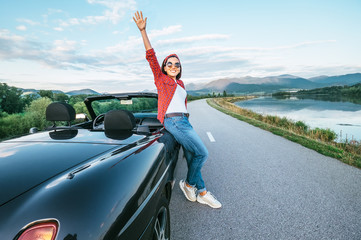 Wall Mural - Happy smiling young woman stay near the cabriolet car on the mountain road