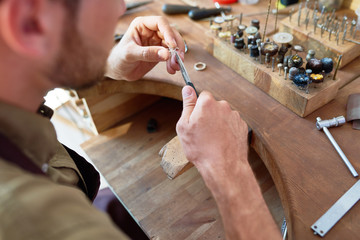 Wall Mural - High angle closeup of jeweler making delicate metal flower in workshop, forming it with tongs against workstation table