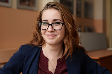 Close-up portrait of a young woman in glasses. A girl with red hair in the classroom. Business woman in training class