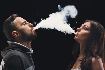 Young couple vaping e-cigarette with smoke on black closeup