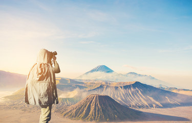 Asian male photographer in coat shooting photos while standing near Mount Bromo, is an active volcano and part of the Tengger massif, in East Java, Indonesia. And with copy space area for your text.