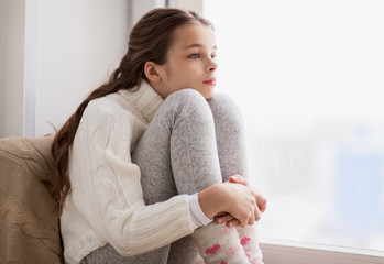 Poster - sad girl sitting on sill at home window in winter