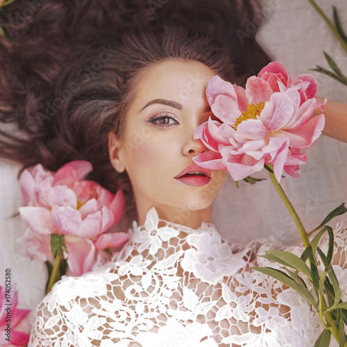 Fotografía Beautiful young woman lies among peonies