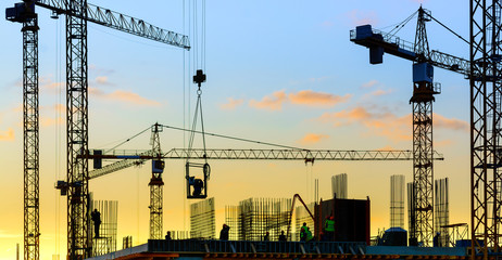 Tower cranes and building silhouette with workers at sunset.