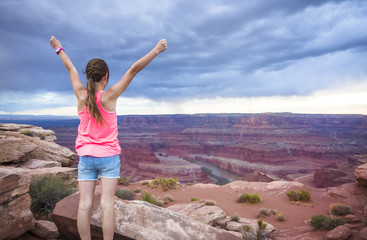 Wall Mural - Young woman viewing the beautiful scenic overlook of Dead Horse Point. She is raising her hands in amazement