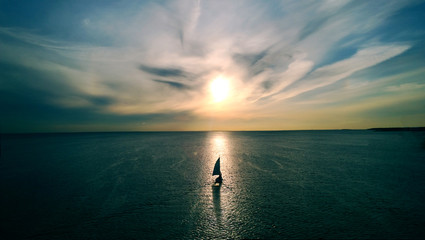 little white boat floating on the water towards the horizon in the rays of the setting sun. beautifu