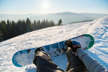 Point of view shot of a female snowboarder lying on the snow on the slope relaxing after riding, enjoying stunning view of winter mountains and sunset POV concept