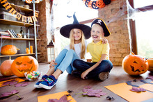 Treat Or Trick! Low Angle Shot Of Junior Blond Kids In Carnival Outfits, Caps, Sitting Down, Near The Window In Halloween Decorated Place At Home, Casual Outfits, Colorful Shoes, Loft Style Of Room