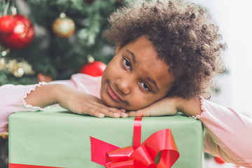 African little girl with gift in front of the Christmas tree. Natural light. 