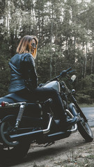 Wall Mural - Outdoor lifestyle portrait of sexy biker girl wearing leather jacket sits on a modern motorcycle, forest road