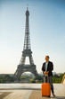 © Suzi Media  - Handsome man woman with orange suitcase standing on Trocadero square. Paris cityscape, view of Eiffel Tower. Travel concept