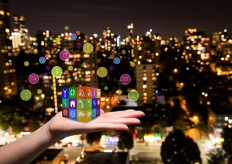 Sticker - hand with applications icons cube on it. Blurred city at night