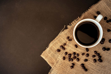 Wall Mural - A cup of coffee and coffee bean grain on sack fabric put on black wood table background include copyspace for add text or graphic