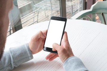 Poster - Modern black smart phone in man hand. Isolated screen for mockup, app presentation. White wooden desk in background.