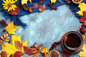 autumn leaves, cup of tea and scarf on blue background