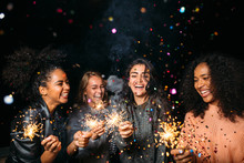 Happy women at night. Laughing friends with sparklers under confetti.