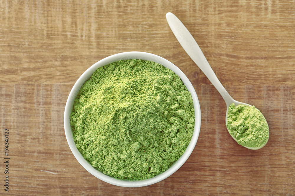 Bowl and spoon with wheat grass powder on wooden table