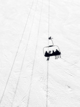 Shadow Of Three Pople Riding A Chairlift On A Groomed Ski Slope