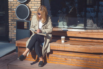 woman sitting at wooden branch in summer cafe and looking at the album. Close up beautiful young blonde painter draws in album in outdoor summer cafe