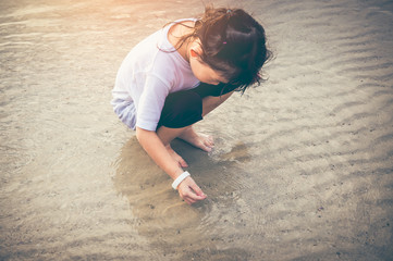 Wall Mural - Charming young girl is looking for sea animals on the beach