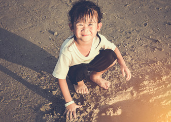 Wall Mural - Happy asian child has fun digging in the sand. Travel on vacation.