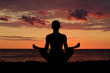 © somemeans - Woman meditating on the beach in lotus position. Silhouette, sunset