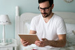 © NDABCREATIVITY - Young handsome man using digital tablet on bed