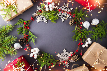 Wall Mural - frame with christmas wreath, gift boxes, branches and snowflakes on dark background top view. merry 
