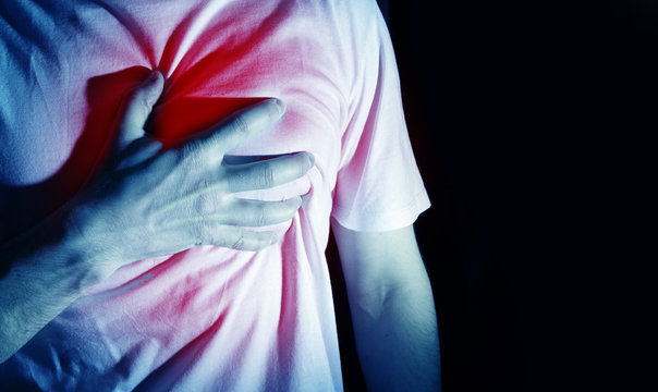 Fototapete - man, guy in a white t shirt on a black background in a blue color hold hands on his heart, heart atack, severe heartache, chest  myocardial infarction