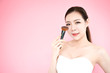 © Nusara - Asian beauty woman with blush brush present product for face on pink background