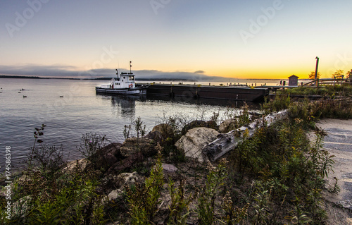 Fototapeta Sunrise Lake Superior. Mały holownik cumował na Jeziornym Wyższym doku z nabrzeżnym wschodem słońca w tle. Narodowy teren rekreacyjny Grand Island. Munising, Michigan.