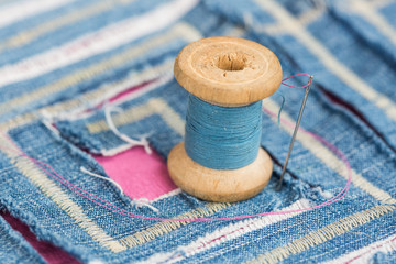 Wall Mural - sewing and embroidery concept - installation of a needle and spool of blue threads over decorated blue fabric with cut pattern, macro of stitching and designer decors in the form of labyrinth