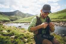 Fly Fisherman Sitting Near A River Tying A Fly