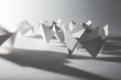 © Catherine MacBride/Stocksy - Folded white paper fortune tellers casting long shadows