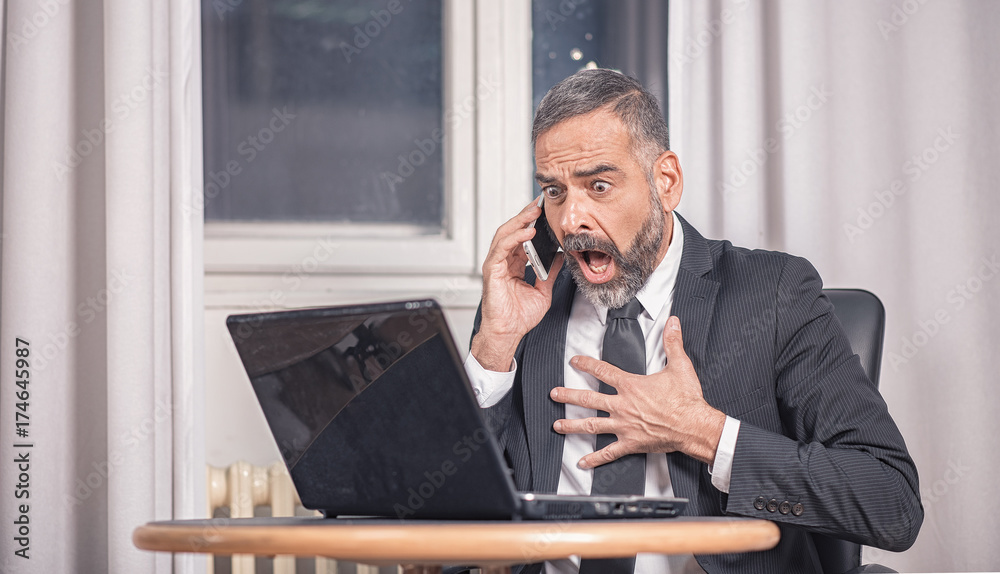 Senior business man shocked with an email he receives on his laptop, office environment