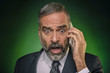 © Teodor Lazarev - Senior business man, in his 50s, shocked over the news he receives on his cell phone, green background