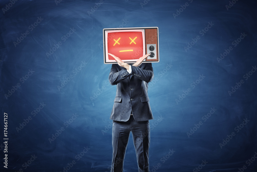 A businessman with a TV on his head showing a red face crosses his hands in prohibiting motion.