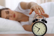 © rogerphoto - Beautiful sleeping woman resting in bed and trying to wake up with alarm clock