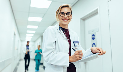 female physician in hospital corridor writing prescription