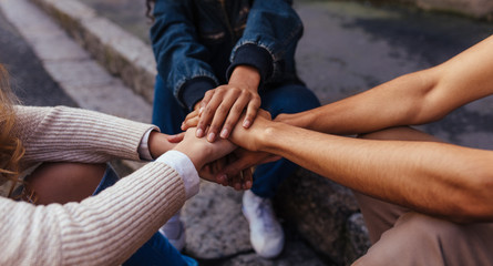 Group of friends sitting together stacking their hands on one an