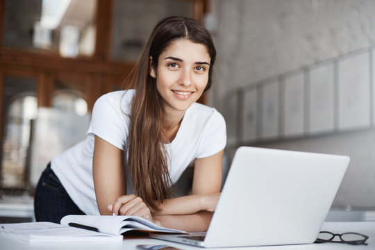Young product design female student working with laptop in library or campus looking at camera smiling. Future is in our hands.