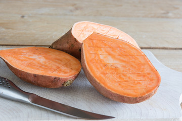 Wall Mural - Raw, orange sweet potato on wood background.  Cut in half